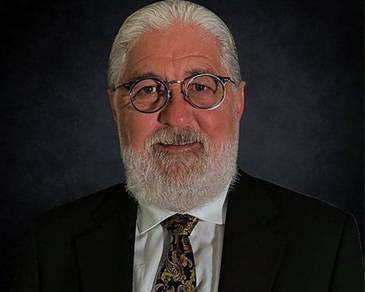 A person with a white beard and glasses Description automatically generated with low confidence