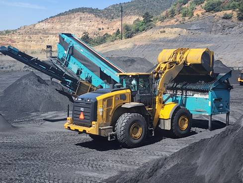 A yellow and blue construction vehicle loading gravel into a truck AI-generated content may be incorrect.