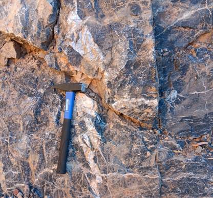 The image shows a black hammer leaning against a rough, textured rock surface. AI-generated content may be incorrect.