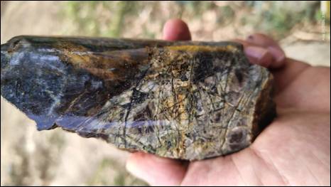 The image shows a hand holding a large, polished, dark green, and shiny gemstone with a pattern of fine lines and a glossy surface. AI-generated content may be incorrect.