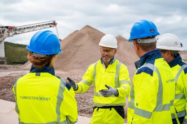 Tungsten West begins production at Hemerdon mine (TUN) The image shows a construction site with workers in high-visibility vests and hard hats, overseeing the movement of large mounds of soil, with a construction crane in the background. AI-generated content may be incorrect.